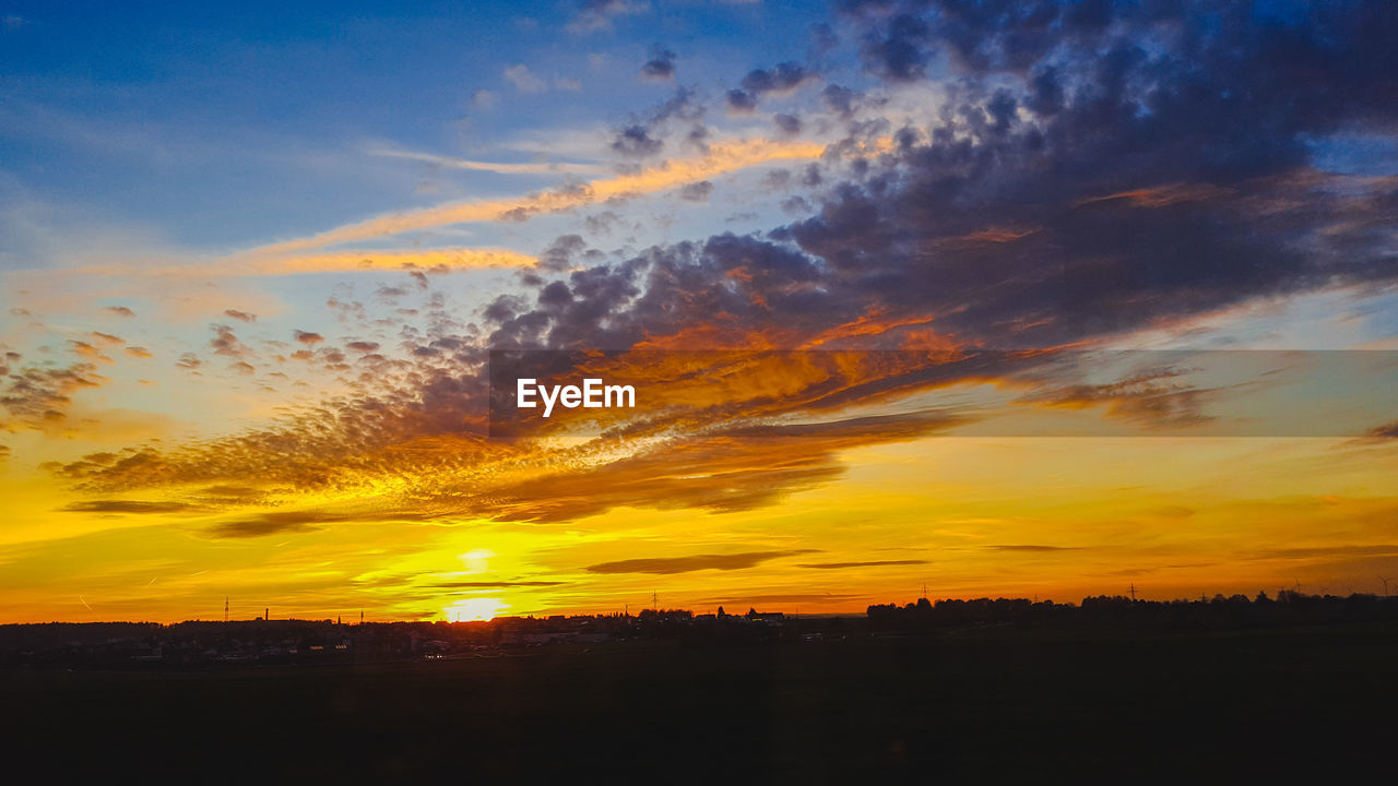 Silhouette trees and cityscape against sky during sunset