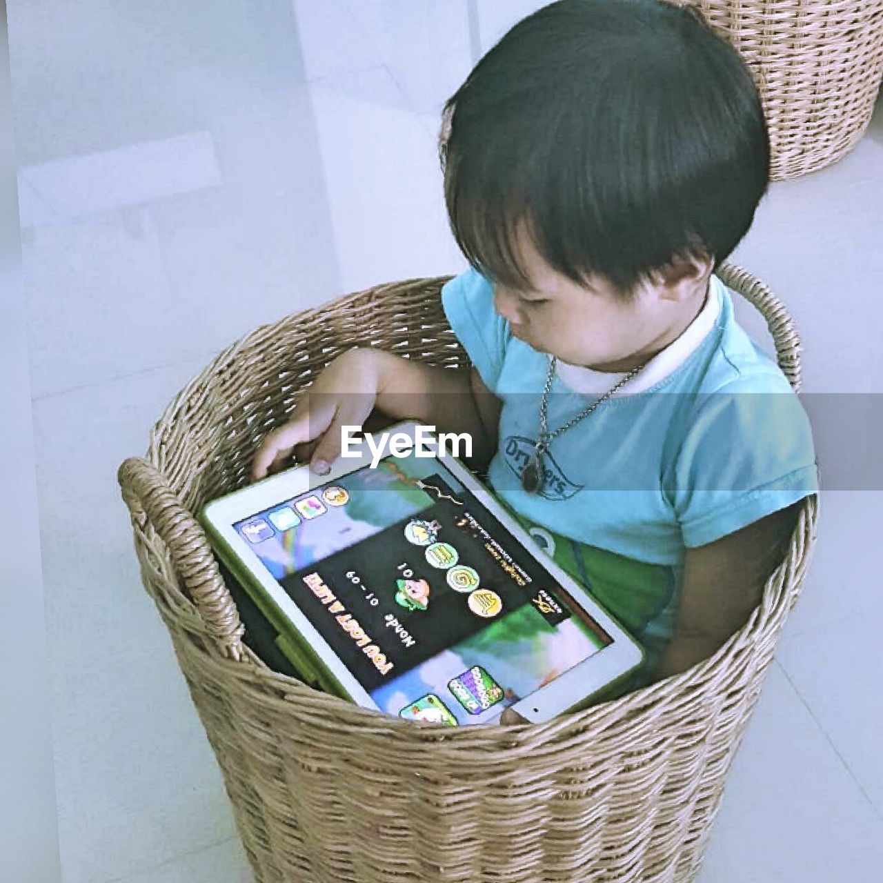 High angle view of child using digital tablet while sitting in wicker basket