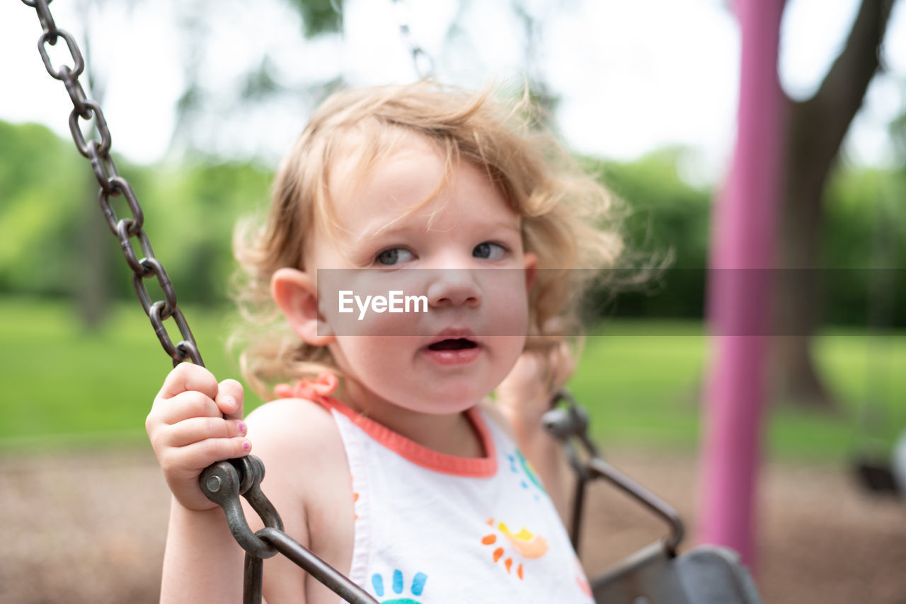 Cute girl looking away while sitting on swing 