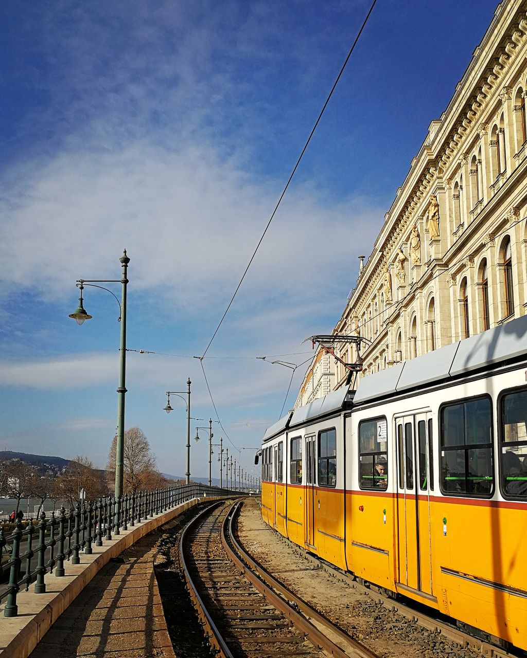 Yellow train on bridge by building against sky