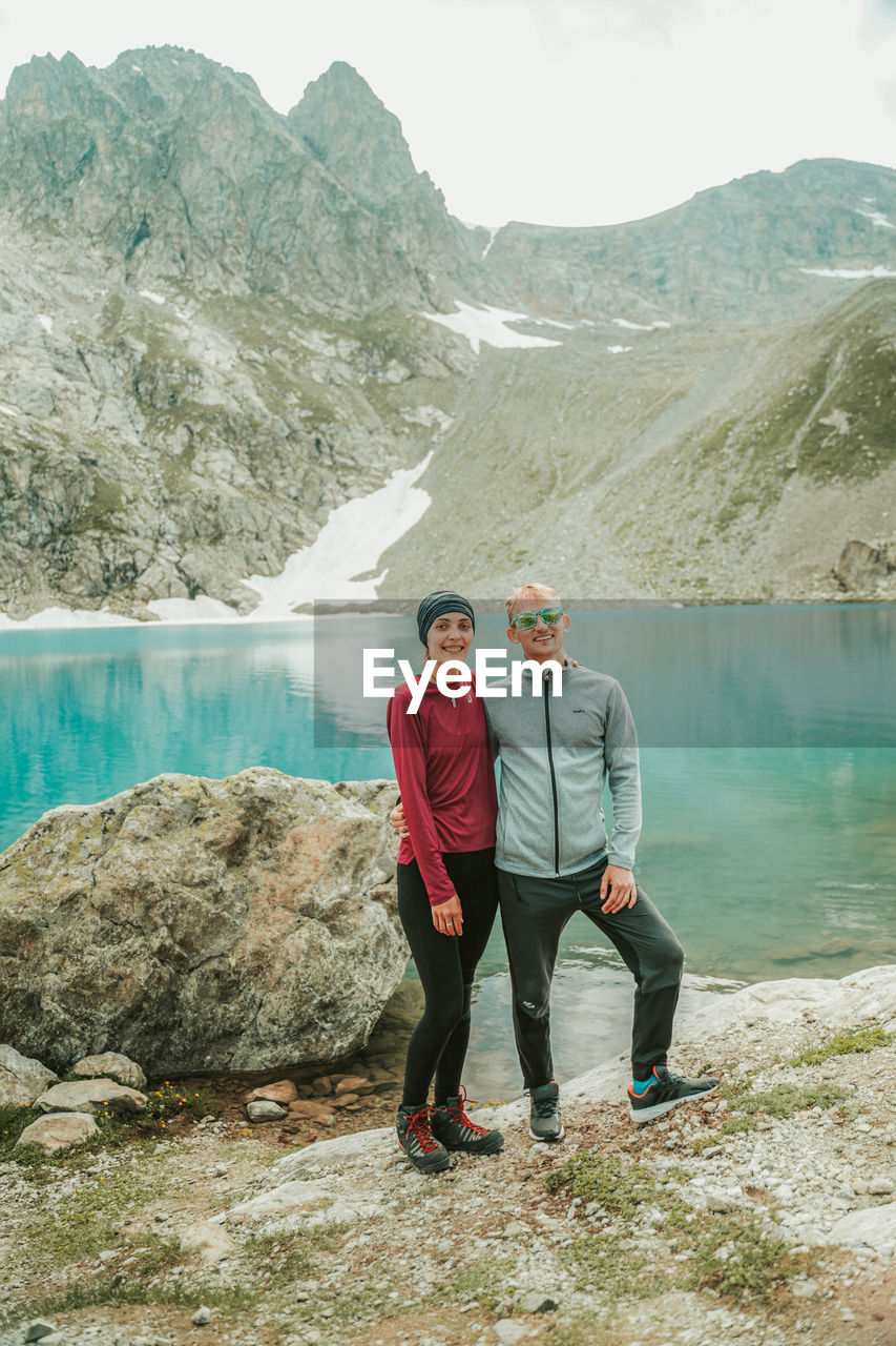 MEN STANDING ON ROCK BY LAKE