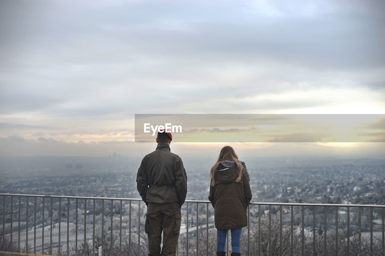 Rear view of man and woman standing by railing against sky