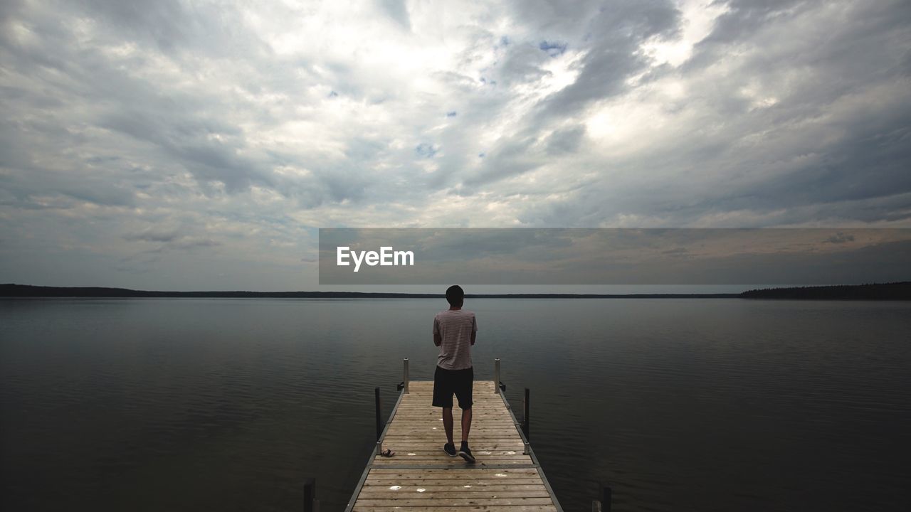 REAR VIEW OF MAN STANDING ON PIER