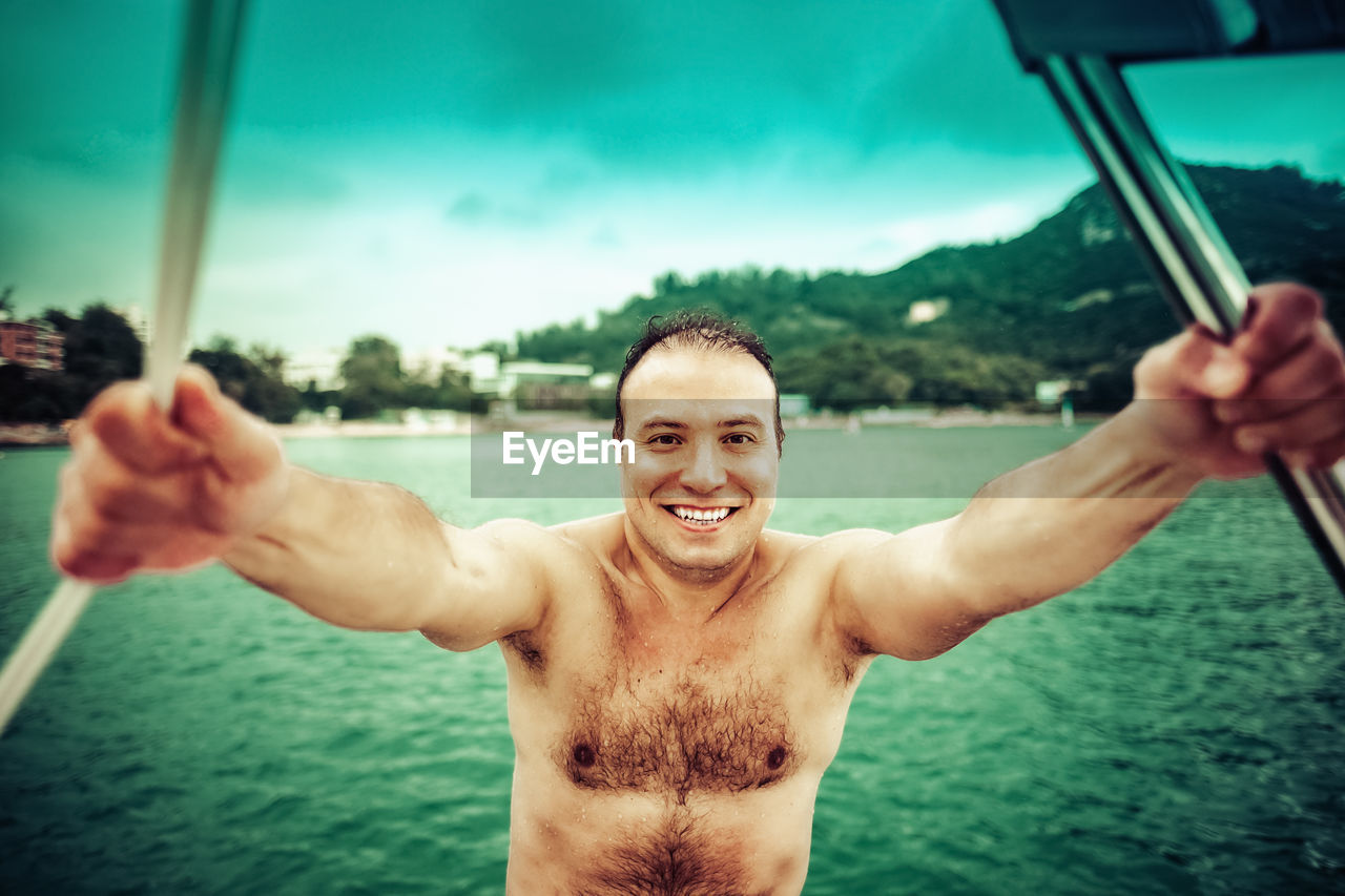 Portrait of happy shirtless man against sea