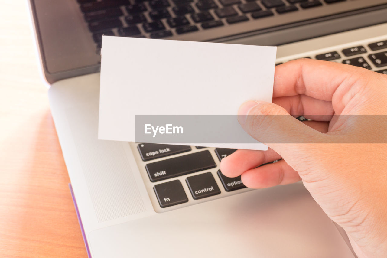 Close-up of woman holding blank paper by laptop on table