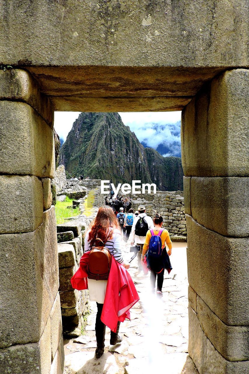 REAR VIEW OF PEOPLE WALKING ON MOUNTAIN AGAINST SKY