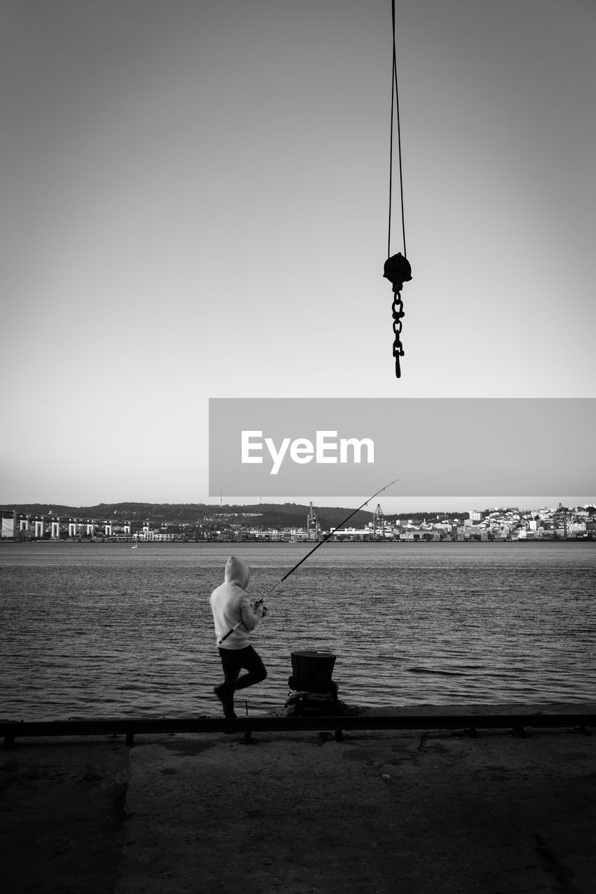 Man fishing in river against clear sky