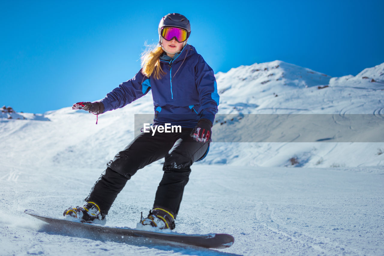 Portrait of woman skiing on snowcapped mountain against clear blue sky