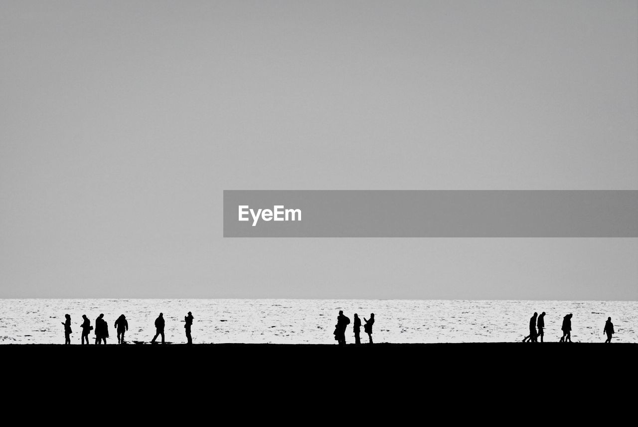 Silhouette people on beach against clear sky