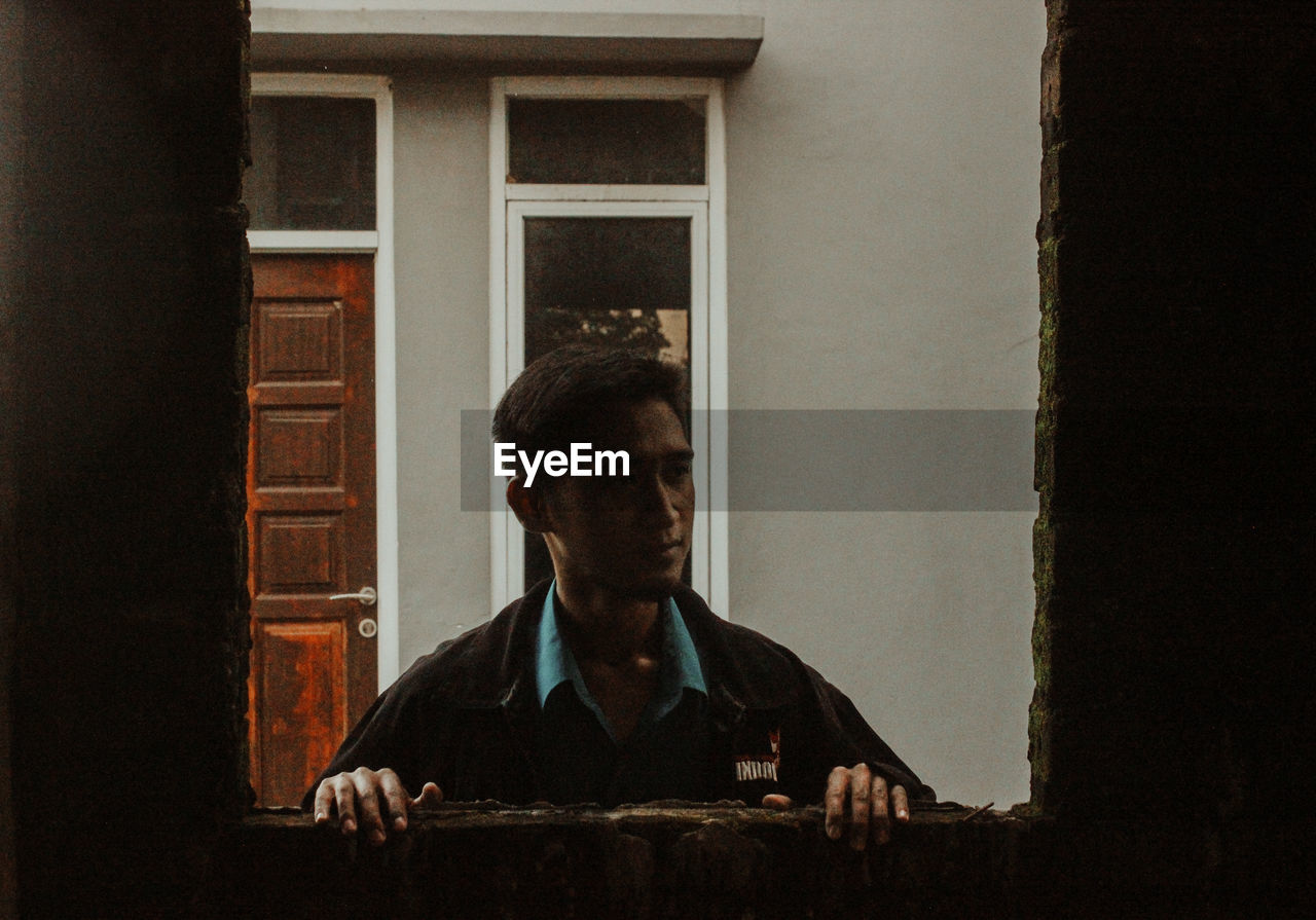 Portrait of man looking through window at home