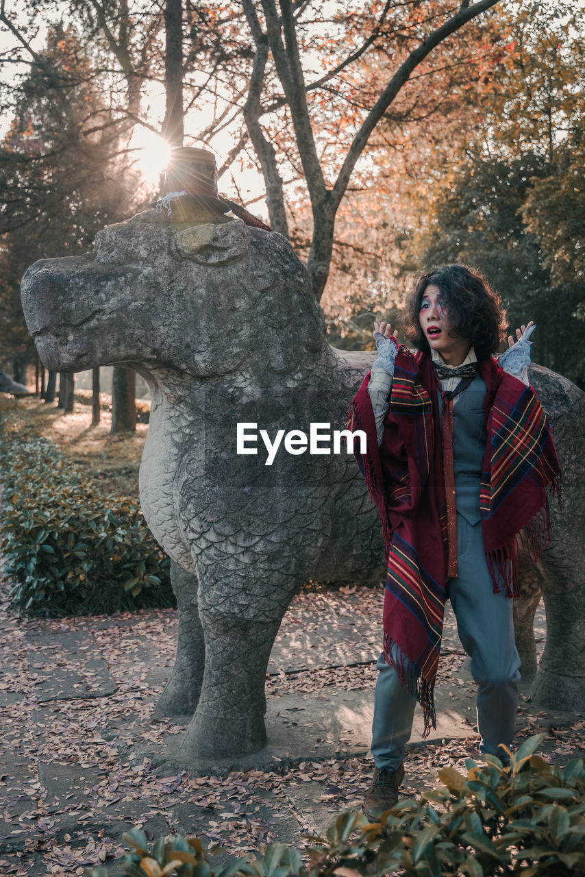 Man cosplaying mad hatter standing by tree against statue during winter