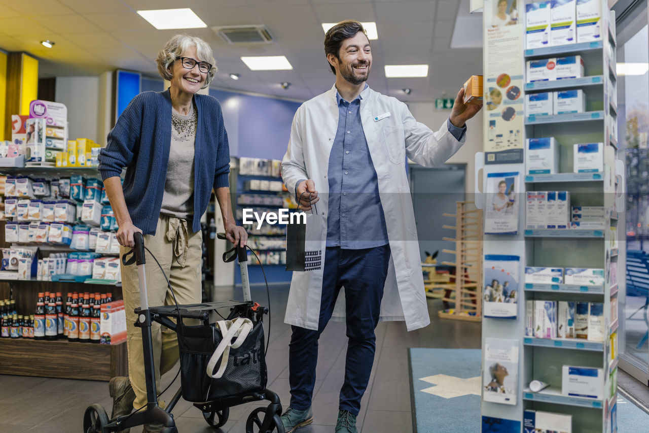 Smiling pharmacist and customer with wheeled walker in pharmacy