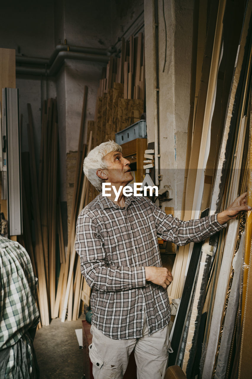 Male senior entrepreneur selecting wood while standing at workshop