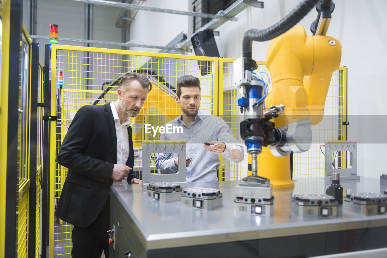 Two businessman observing industrial robots in factory