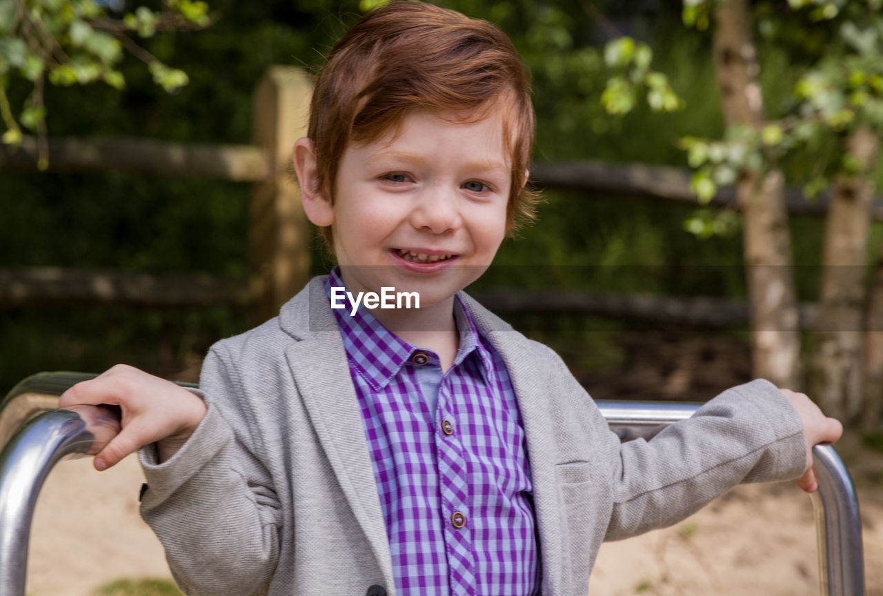 Portrait of cute boy standing on merry-go-round at playground