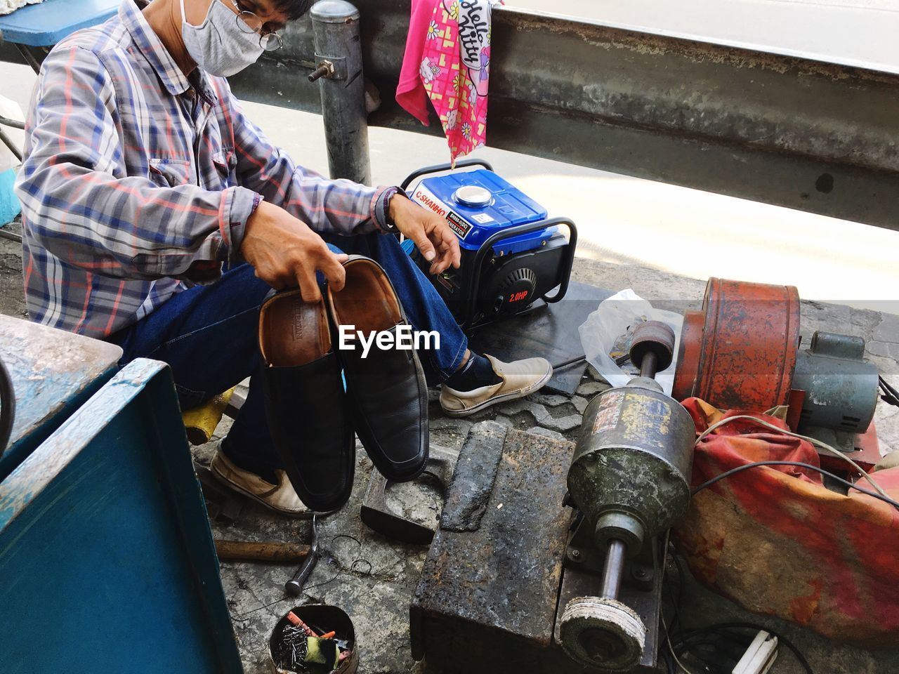 Cobbler holding shoes while sitting on street