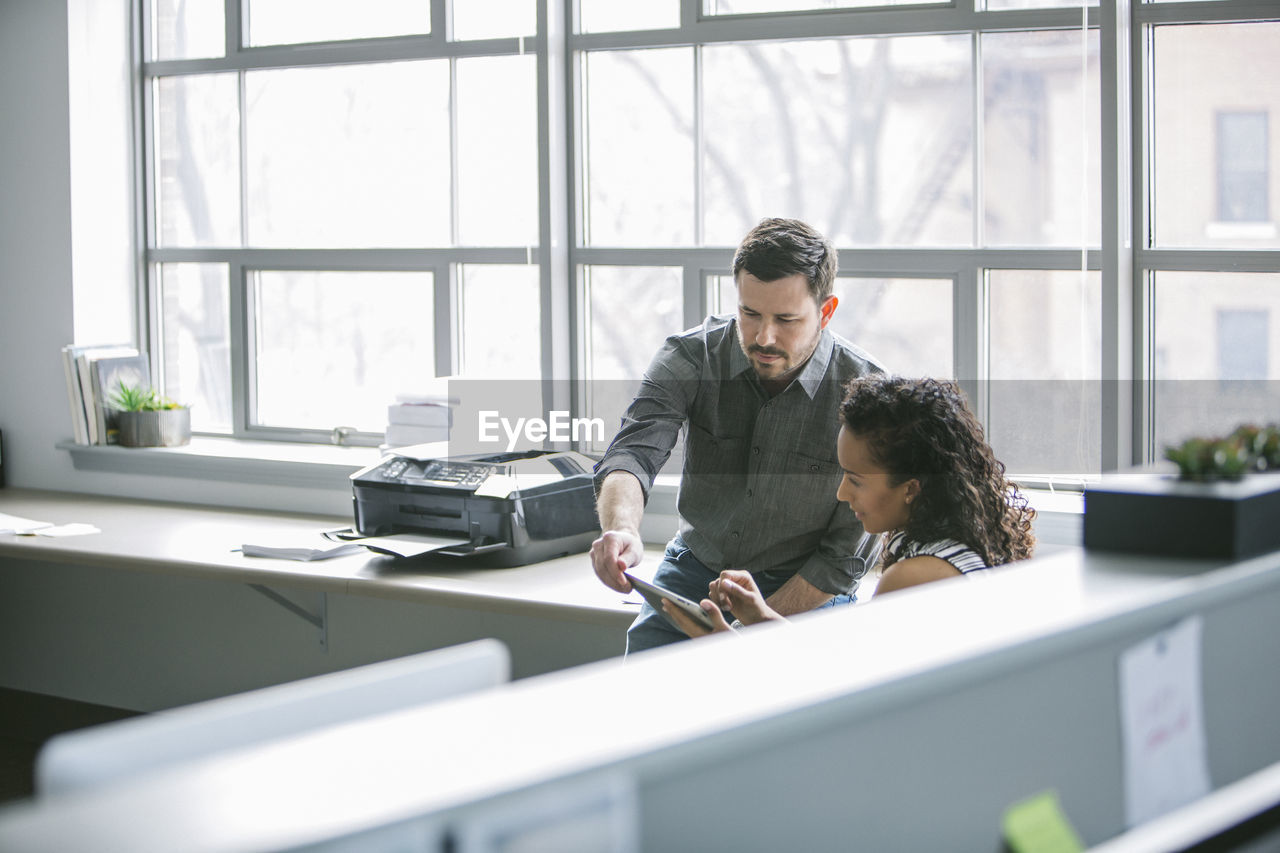 Colleagues using tablet computer while sitting at desk in office