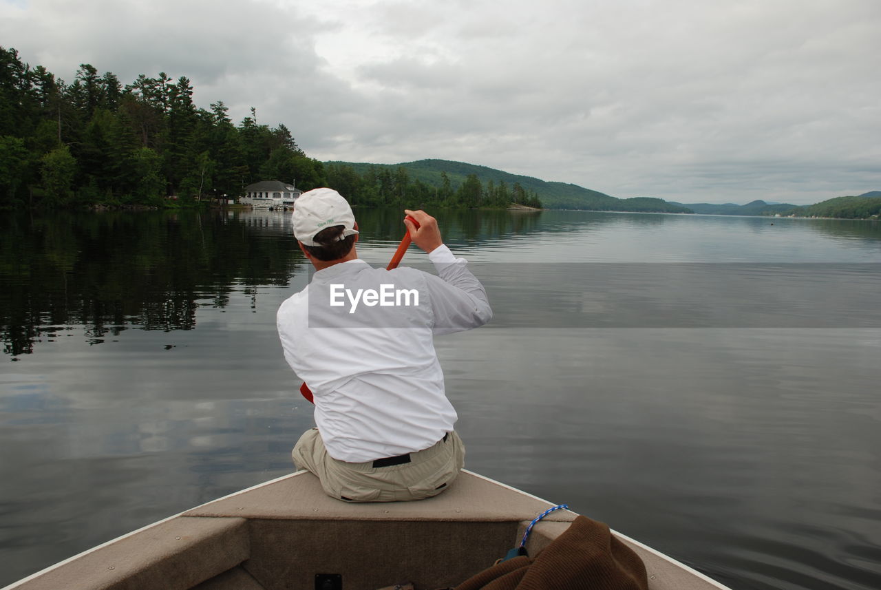 Rear view of man sitting on boat in river against sky