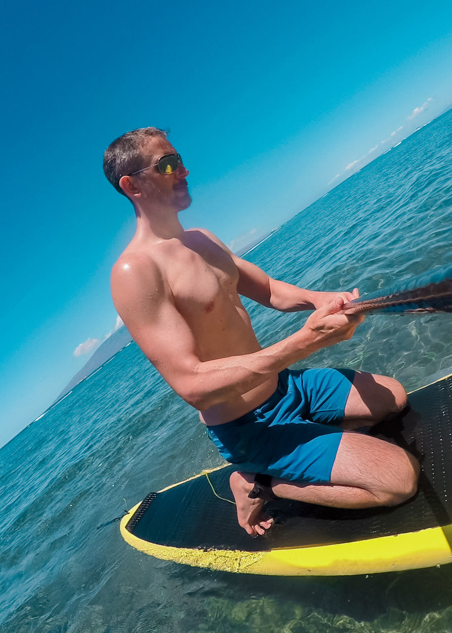 Tilt image of man paddleboard at sea against blue sky