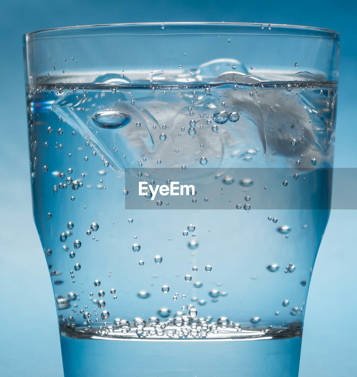 Close-up of water with ice cubes in glass against blue background