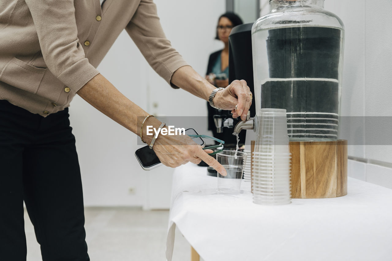 Midsection of mature entrepreneur filling water in glass