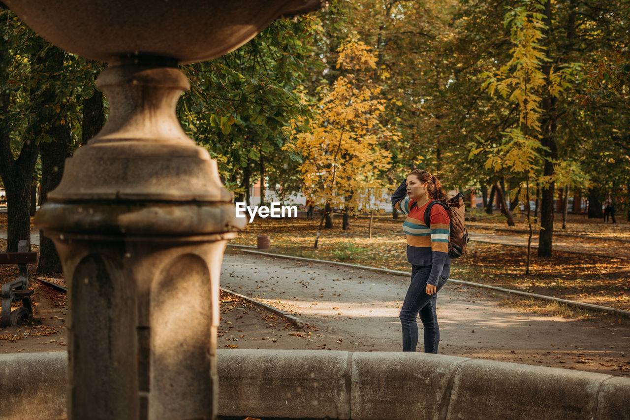 Young plus size traveler girl with backpack traveling along europe autumn city, fall park. solo 