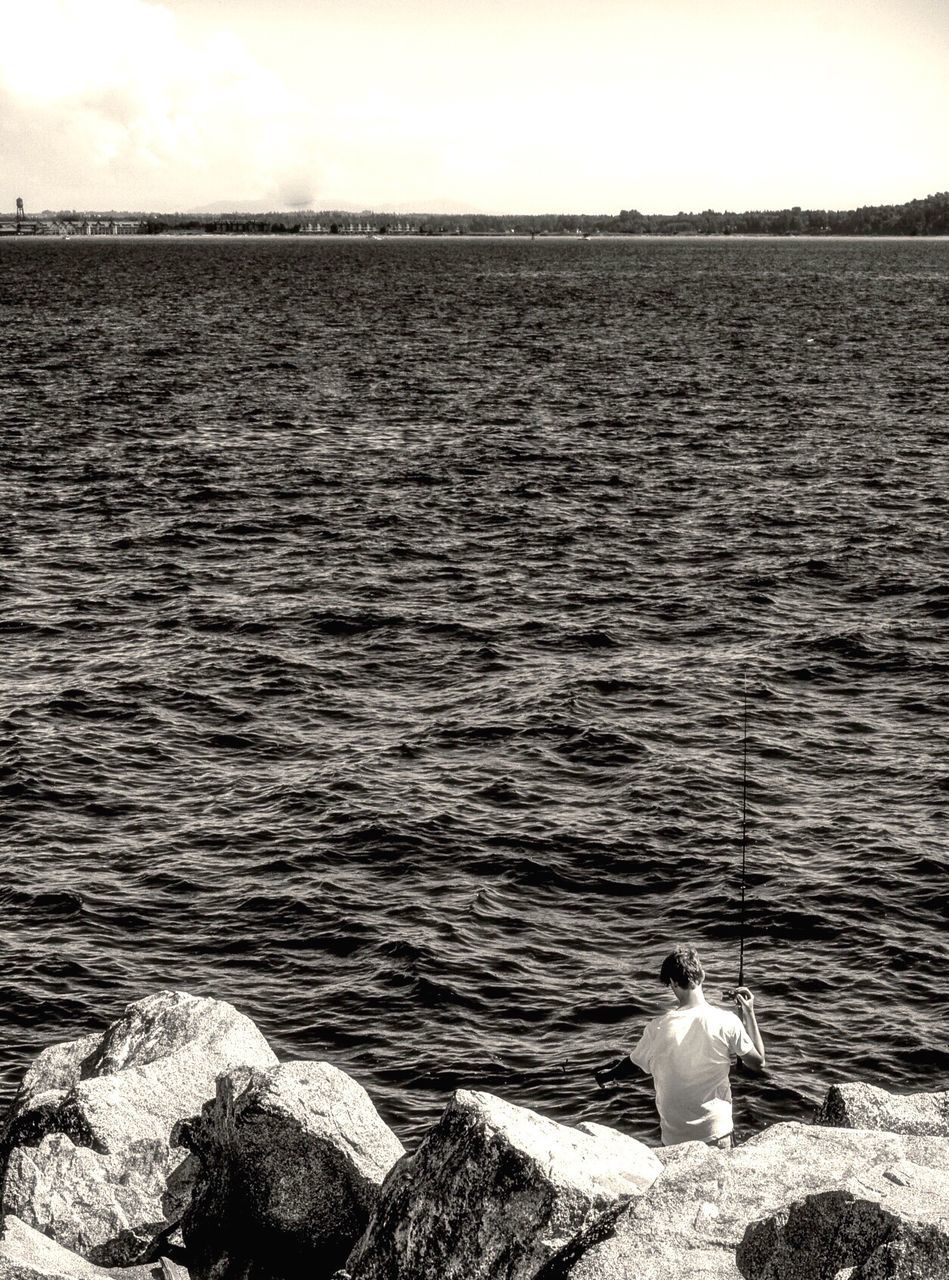 High angle view of man fishing at rocky beach against sea