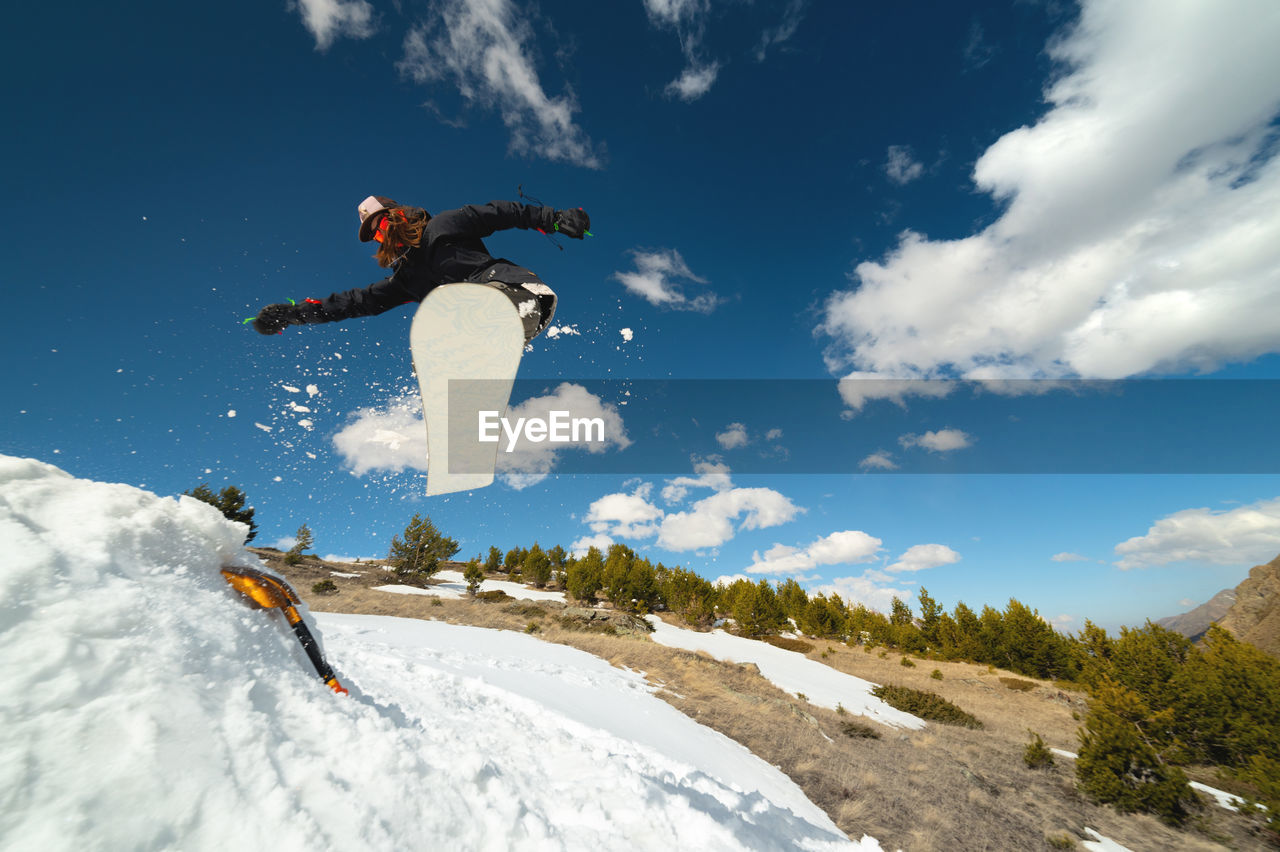 Snowboarder woman jumping from a kicker springboard from the snow on a sunny day in the mountains