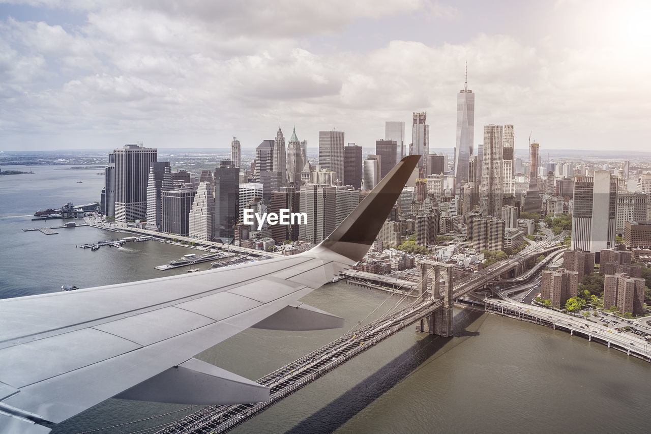 Cropped image of airplane wing flying over river by sea