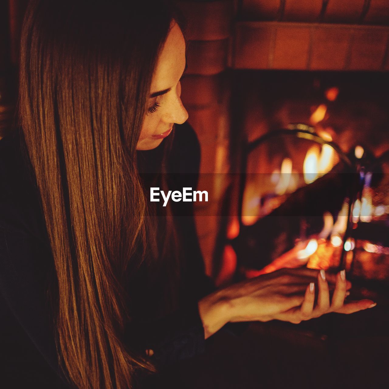Woman with long hair sitting by fireplace at home
