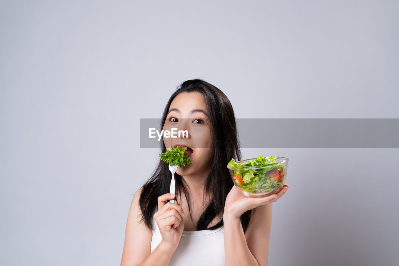 PORTRAIT OF YOUNG WOMAN HOLDING ICE OVER WHITE BACKGROUND