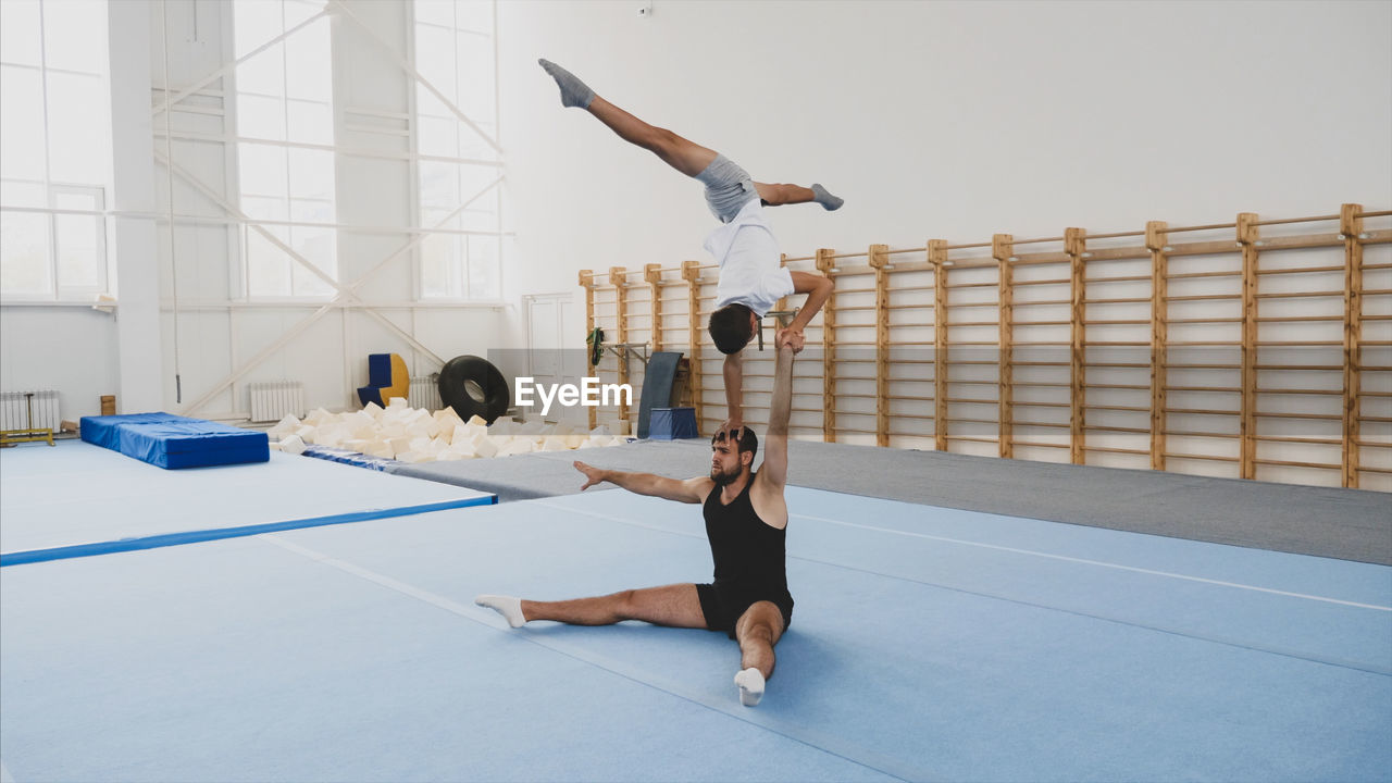 Instructor with teenage boy practicing gymnastics in club