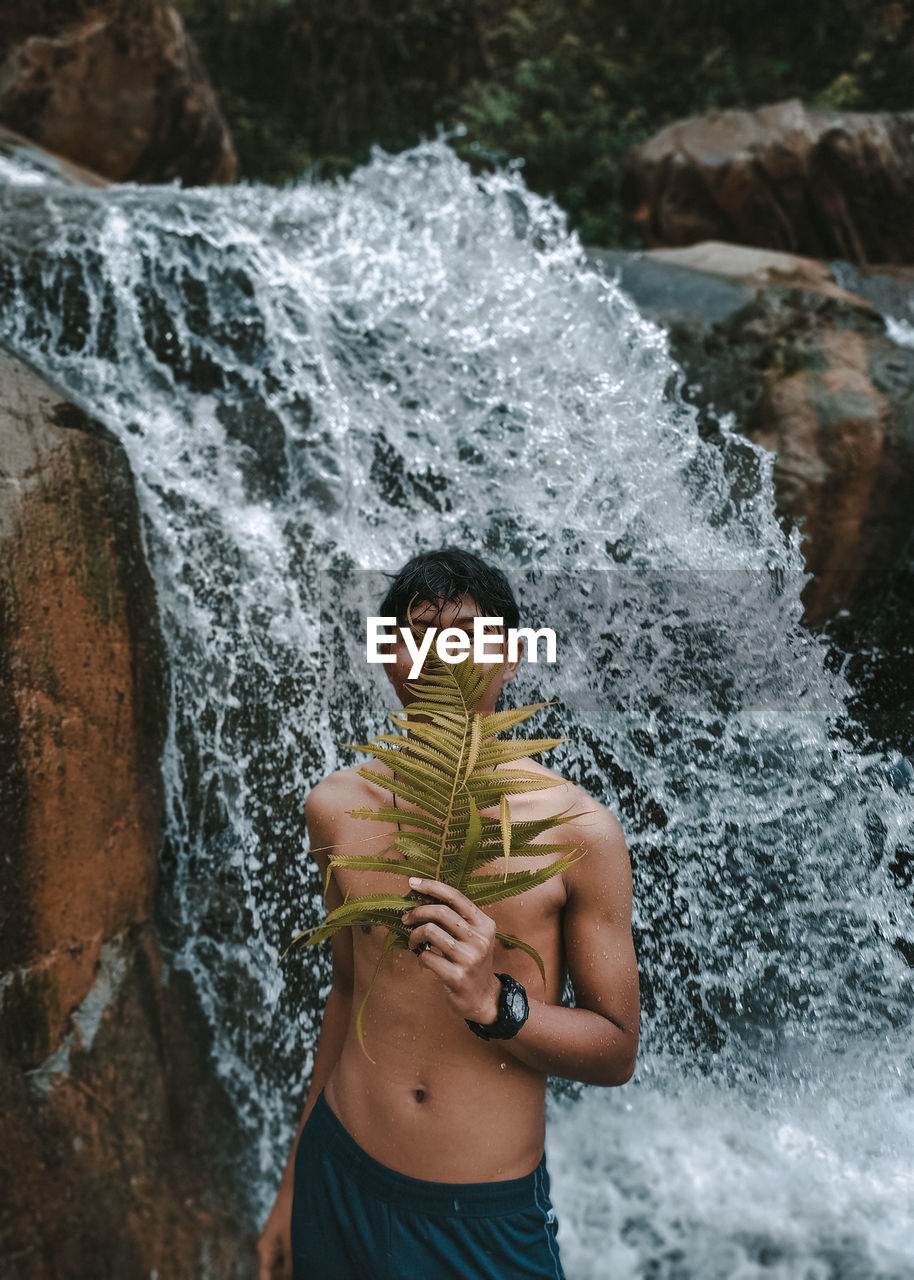 Man standing on rock against waterfall