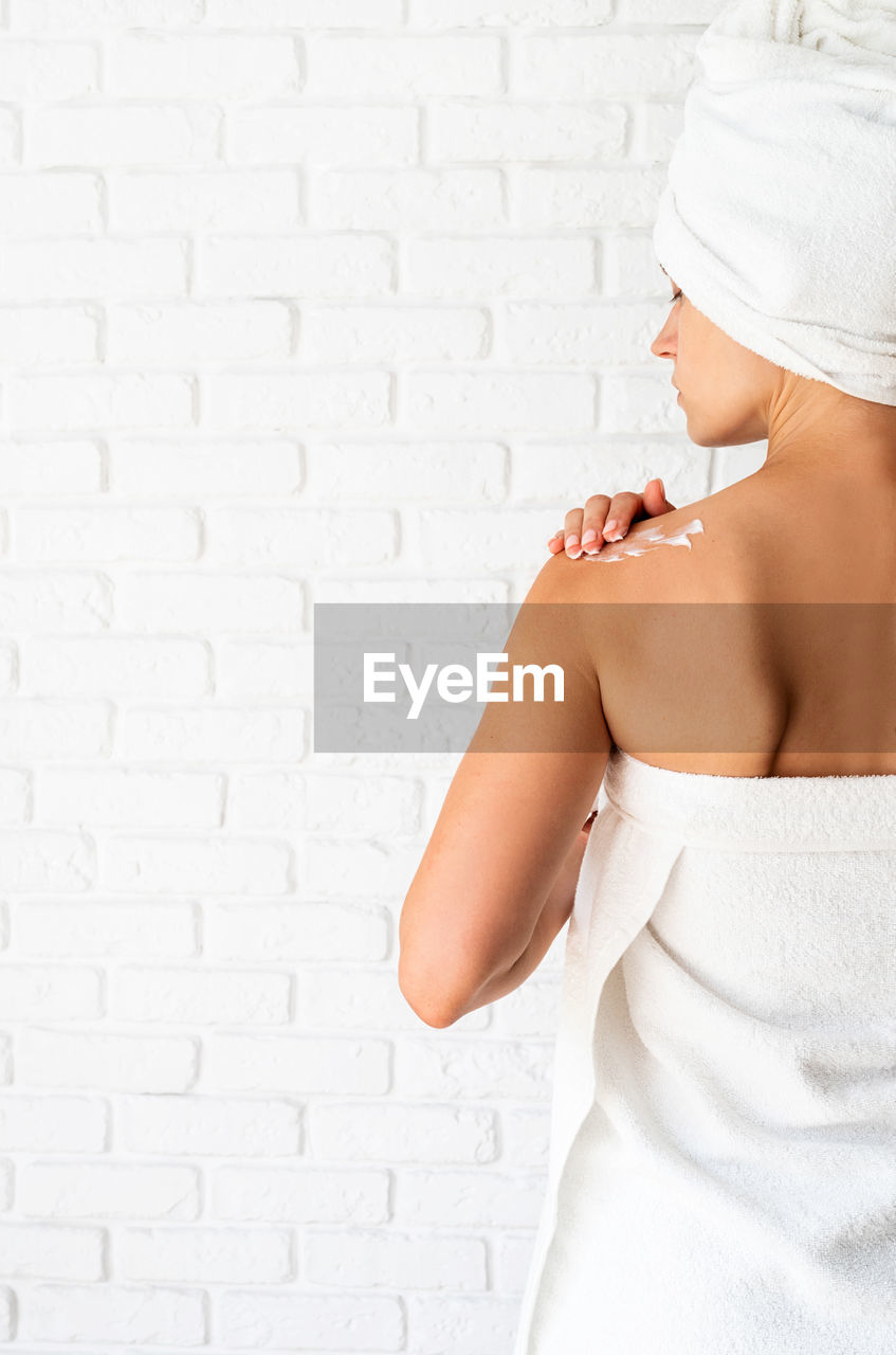 Rear view of a young woman applying cream on her shoulders. spa and beauty. natural cosmetics