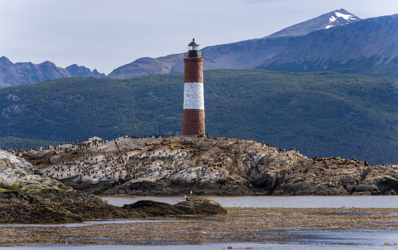 lighthouse by sea against mountains