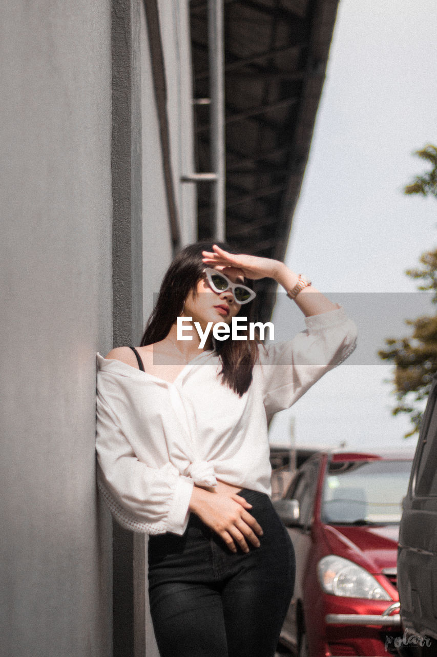 Young woman wearing sunglasses standing against car