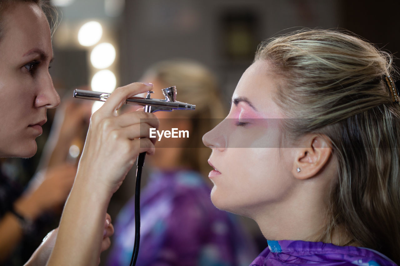 Make-up artist spraying make up on woman at studio