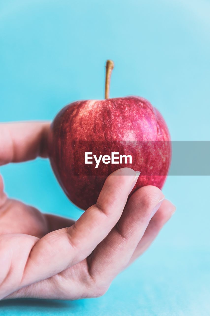 Close-up of hand holding apple against blue background