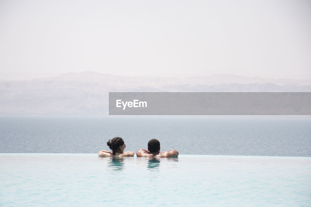 Rear view of couple in infinity pool against sea