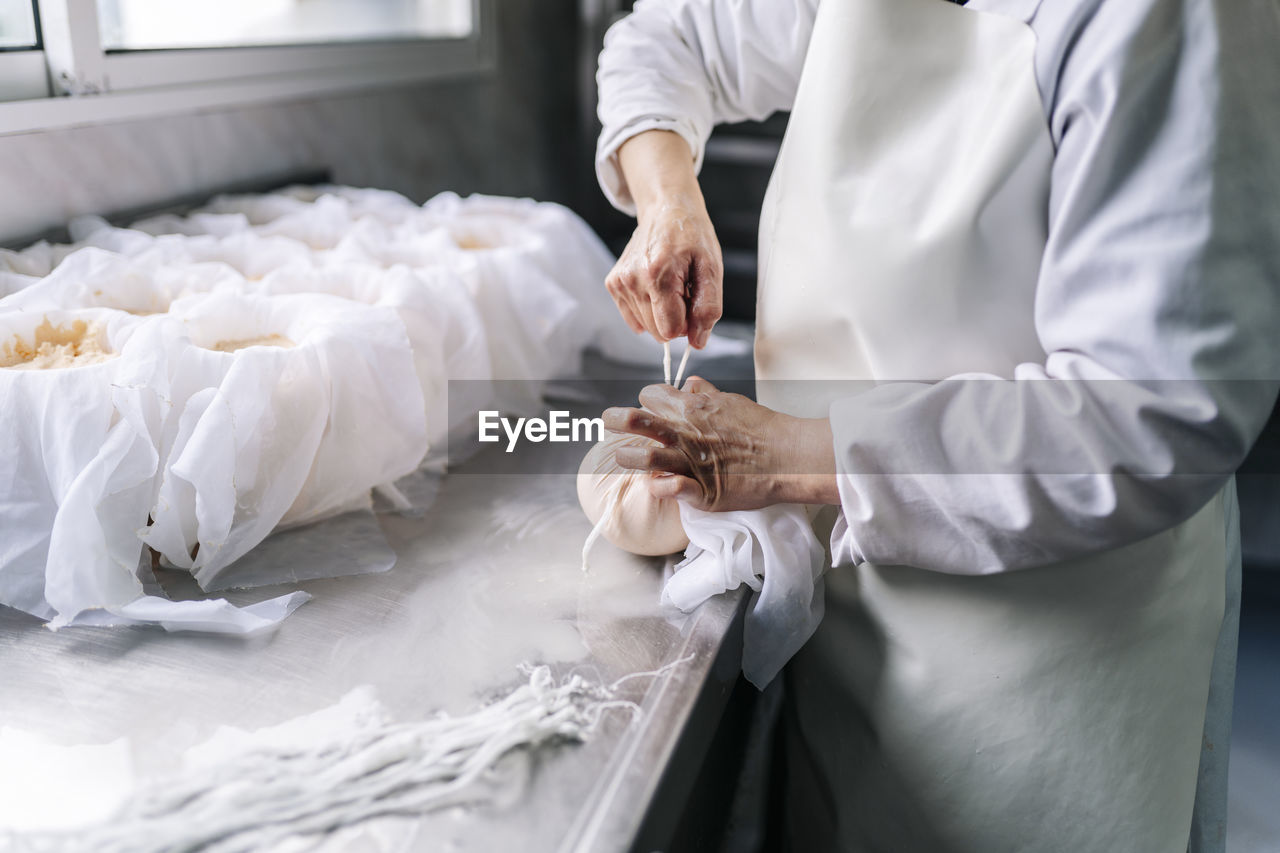 Skilled chef wrapping cheese in cloth at factory