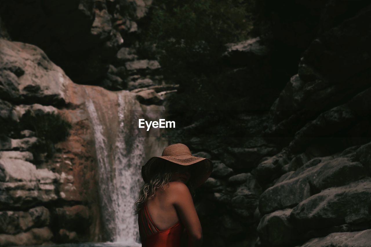 Side view of woman standing against waterfall