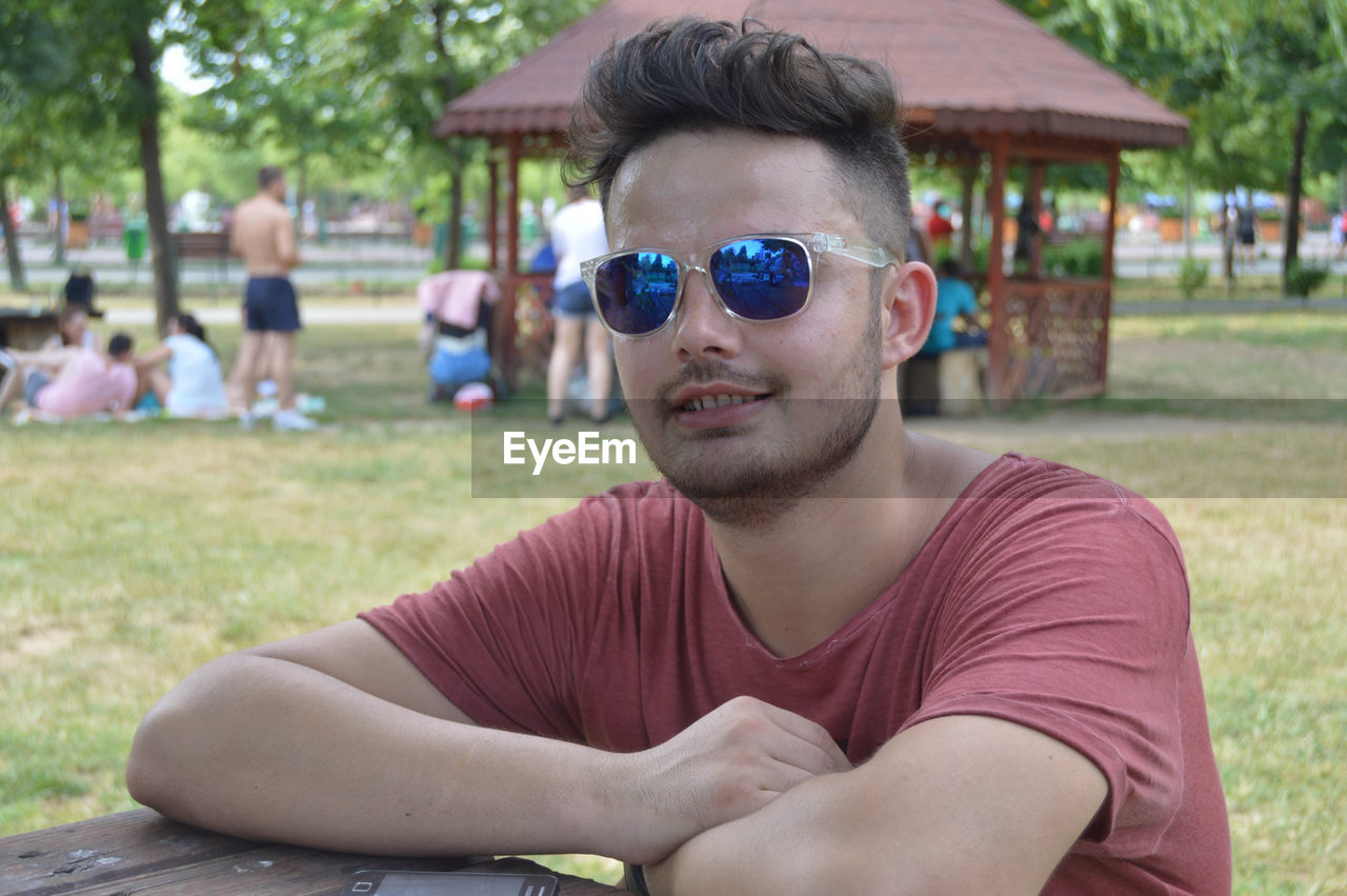 Portrait of young man in sunglasses sitting at park