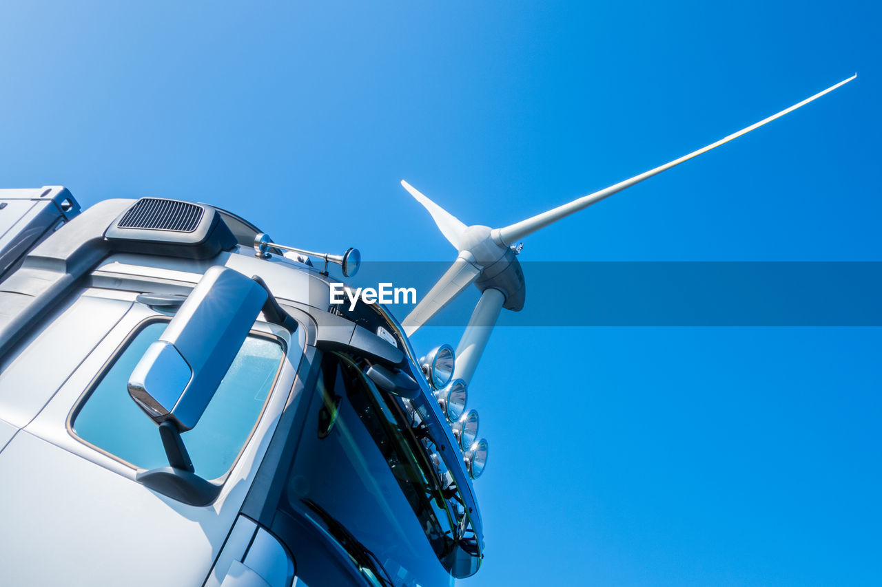 Low angle view of truck and wind turbine against clear blue sky