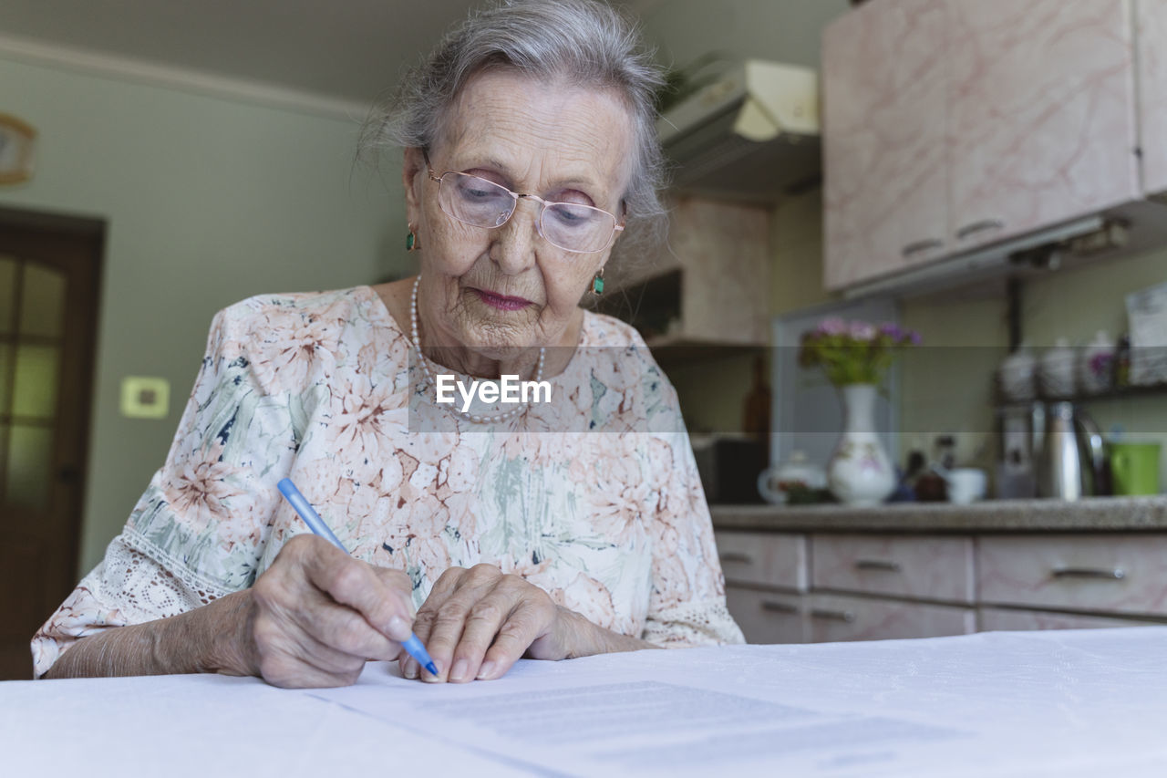 Senior woman with eyeglasses signing home insurance papers on table