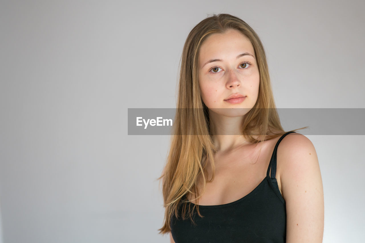 Portrait of an attractive teenage girl wearing camisole posing looking at camera on grey background