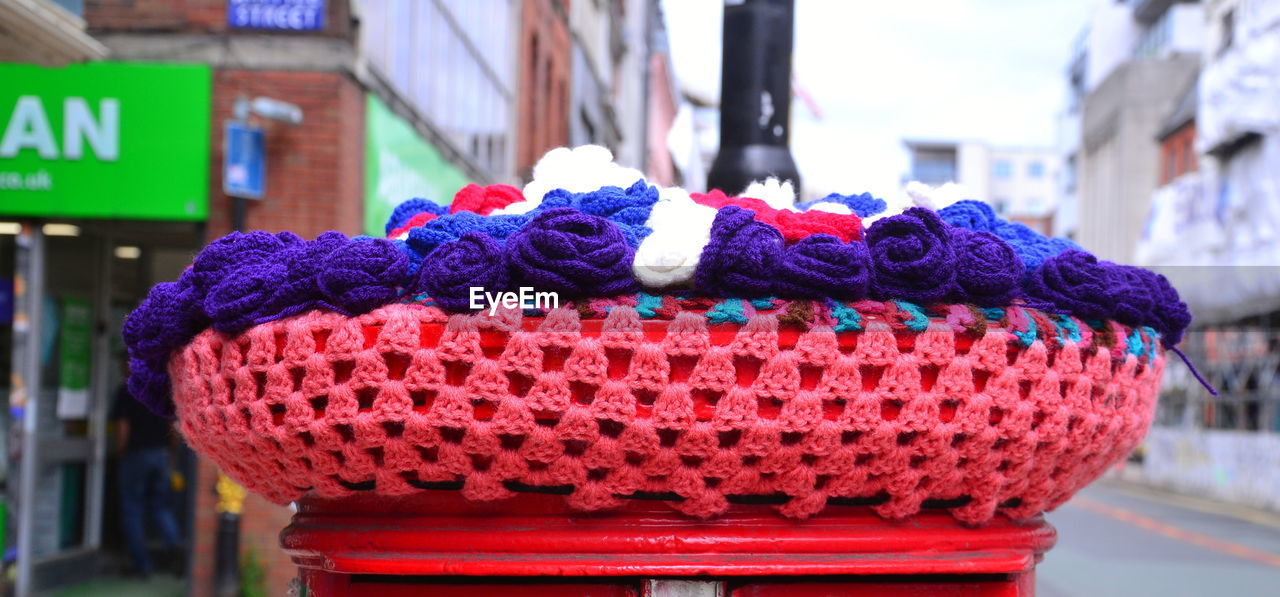 focus on foreground, architecture, red, day, city, wool, multi colored, street, no people, craft, building exterior, crochet, outdoors, textile, close-up, built structure, art