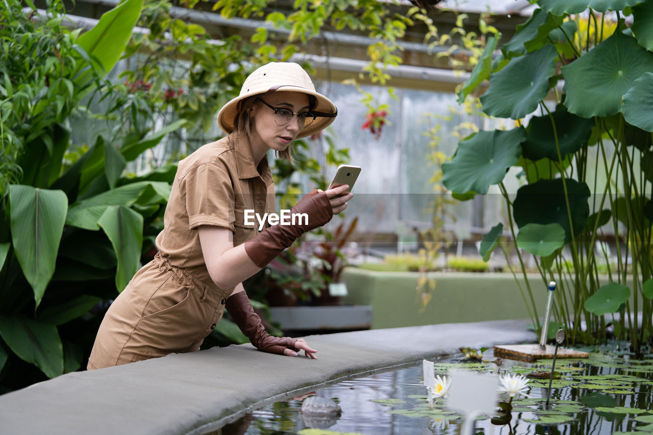 Side view of woman photographing while standing by plants 