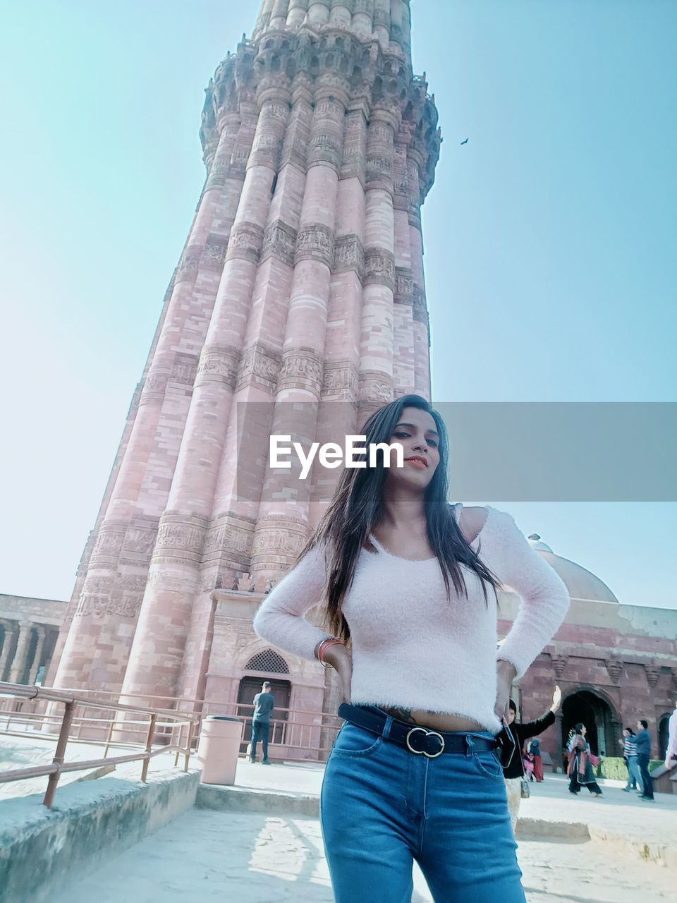 one person, blue, architecture, young adult, women, adult, long hair, standing, three quarter length, front view, travel destinations, portrait, travel, built structure, city, hairstyle, sky, nature, tourism, fashion, smiling, casual clothing, tourist, day, clothing, emotion, brown hair, lifestyles, looking at camera, happiness, building exterior, copy space, outdoors, leisure activity, looking, clear sky, tower, city life, sunny, vacation, trip, holiday, history, sunlight