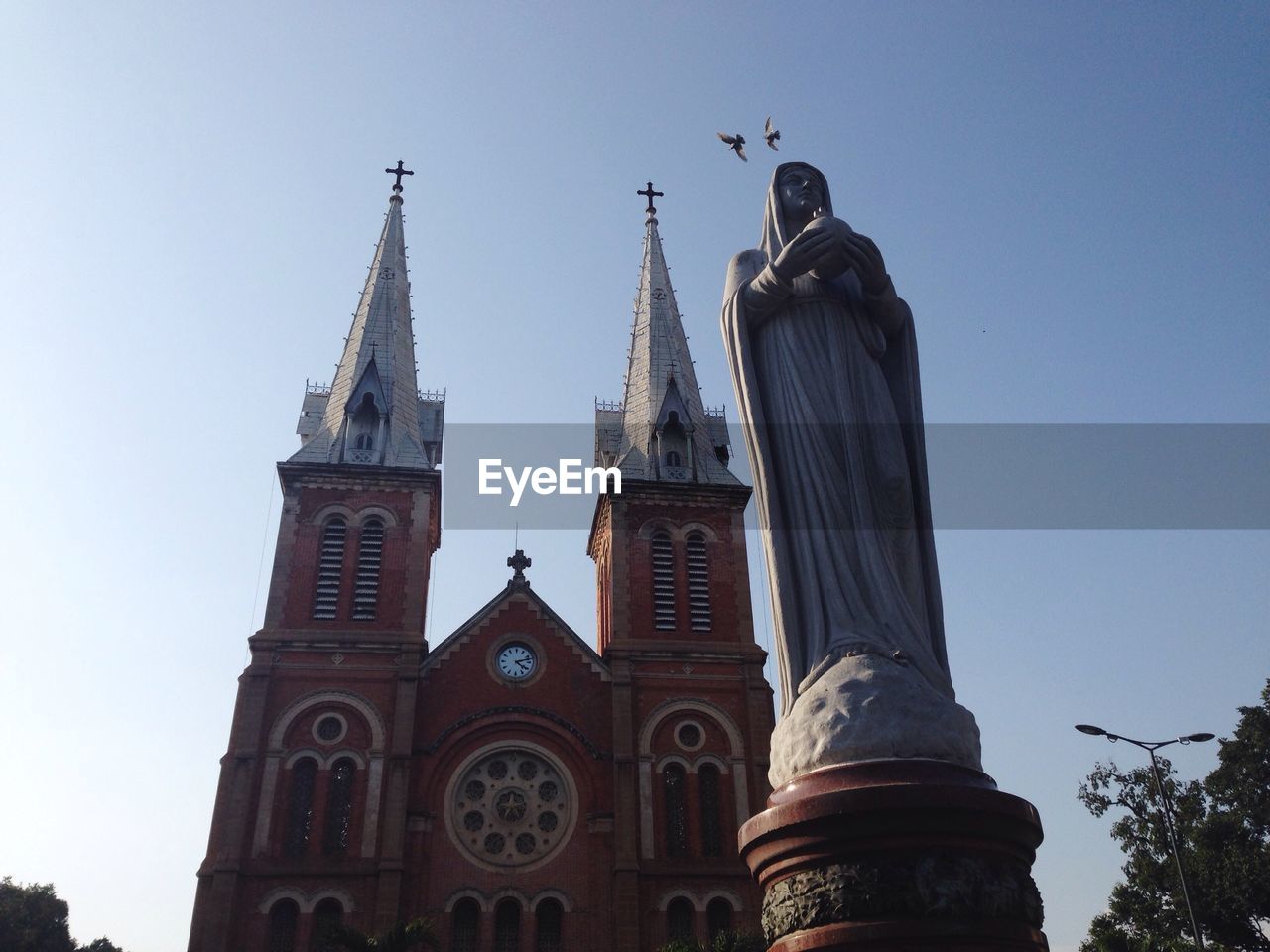 Low angle view of virgin mary statue by church against clear sky