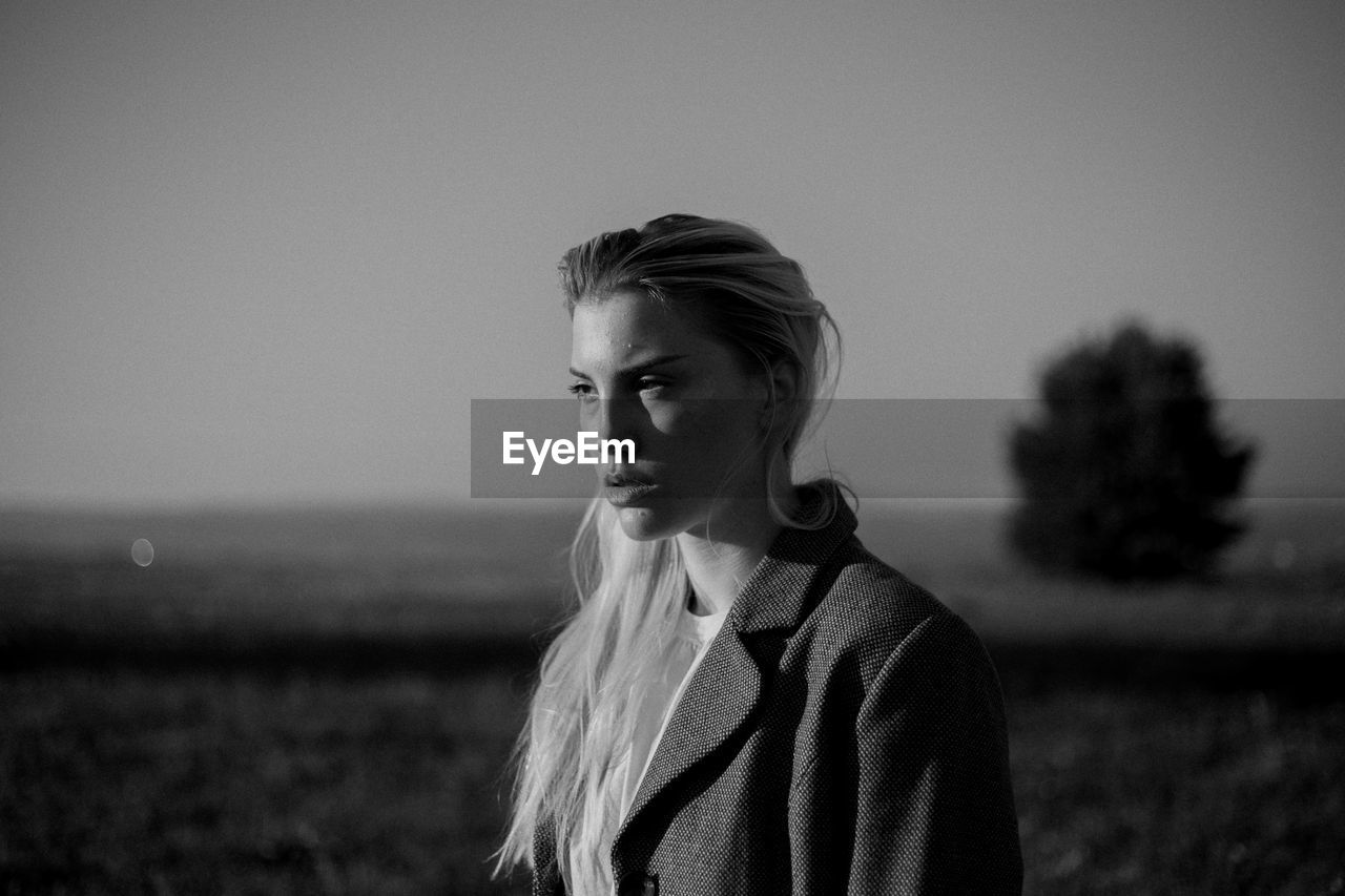 Portrait of young woman looking away on field against sky